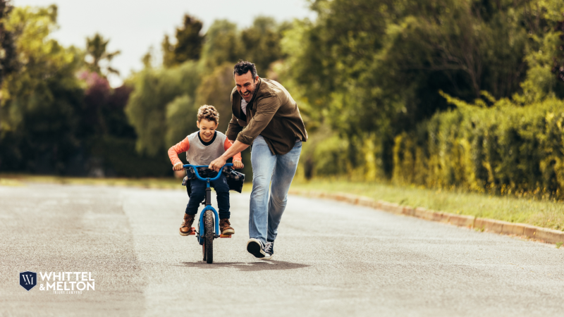 A father helps his young son ride a bike on a sunny day. 