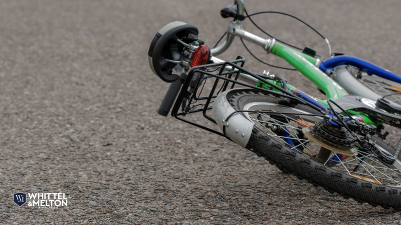 A child's bicycle with training wheels lies on its side on the pavement after an accident.