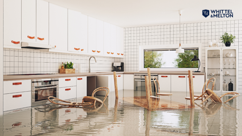 Flooded kitchen with water covering the floor and overturned chairs, symbolizing damage caused by hurricanes or storms. Whittel & Melton law firm logo in the top right.